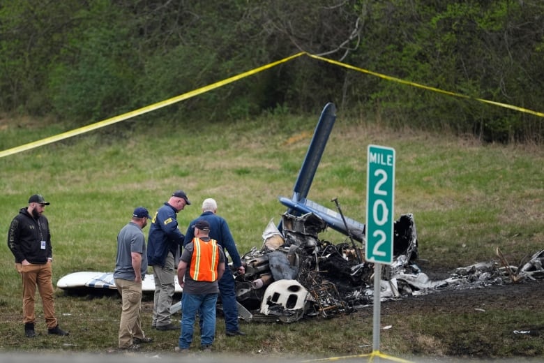 A team of people surround the wreckage of a small plane on grass.