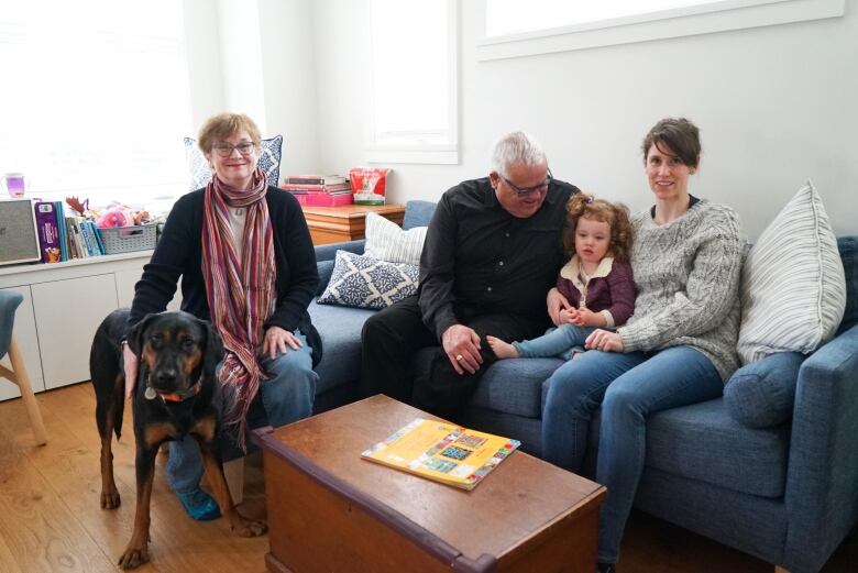 Family of four sitting on a blue couch and a dog. 