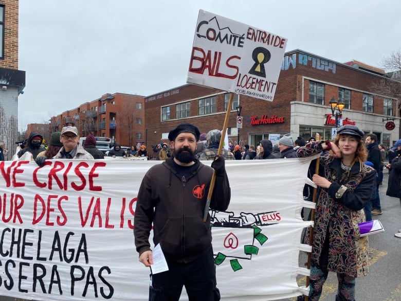 Two people stand in a street with signs.