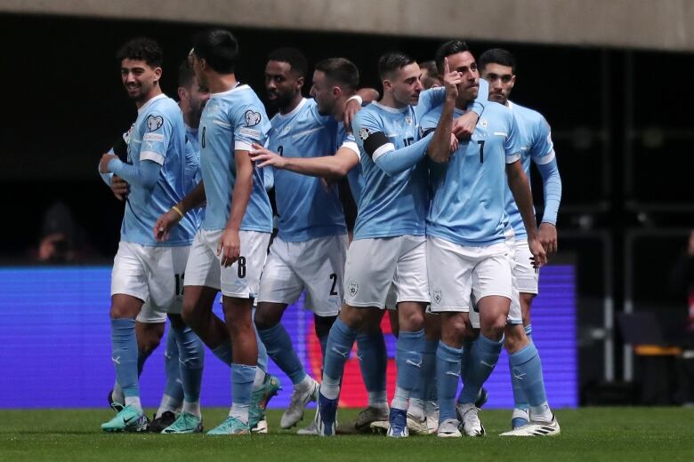 A group of male soccer players celebrate a goal.