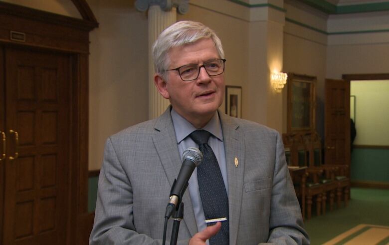 A man in a grey suit standing in a government lobby. 