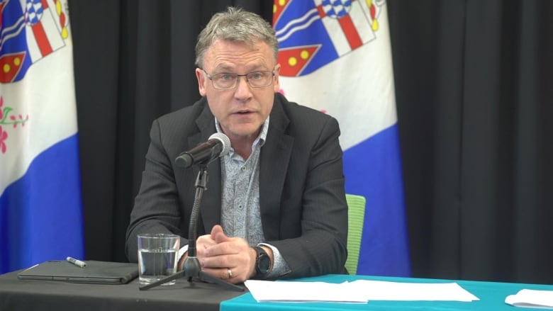 A man sits at a table speaking into a microphone.