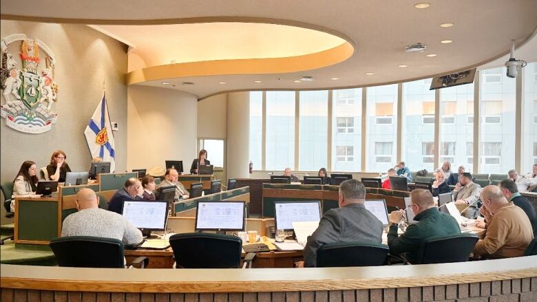 A warm-coloured room is shown with lots of windows and a number of people sitting at computers in a circle.