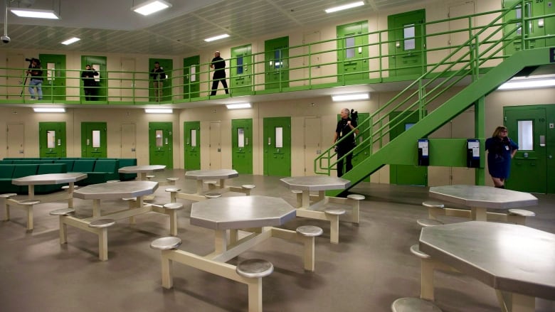 The inside of a jail with green doors and metal tables. 