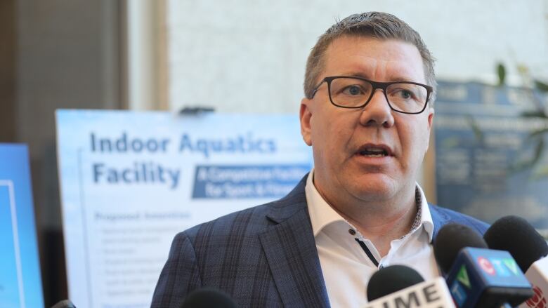 A man in a blue suit jacket and white shirt speaks to reporters. 