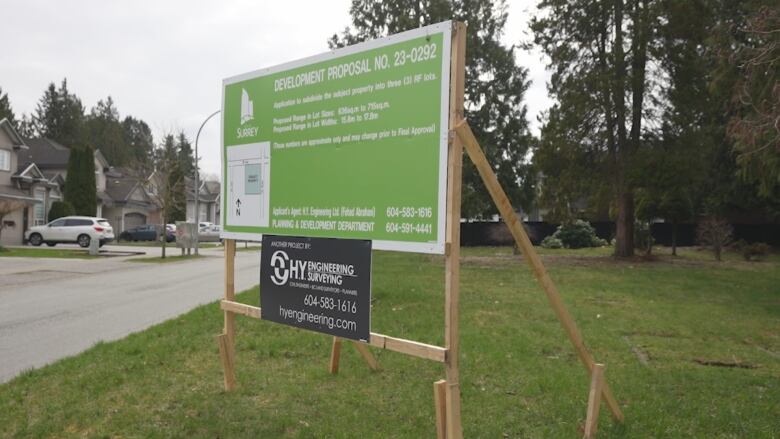 A large billboard in a large suburban lot describes that the land is to be subdivided into three houses.