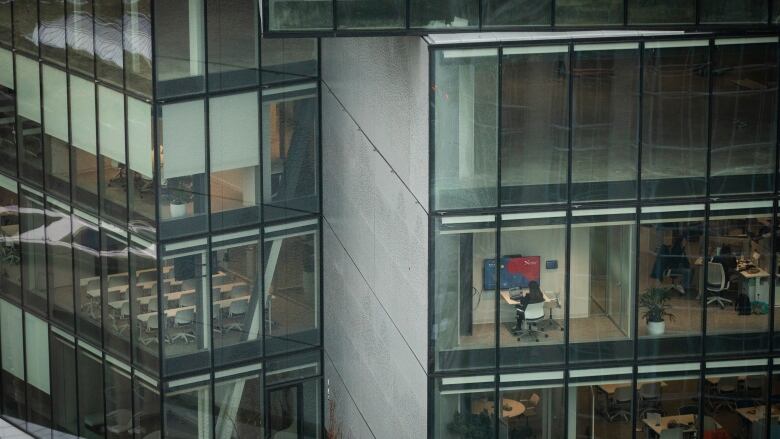 An office building is shown. A worker sitting at a desk is visible through one of the windows.