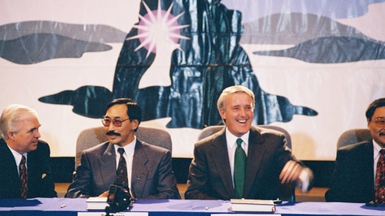 Two men in suits sit at a head table.