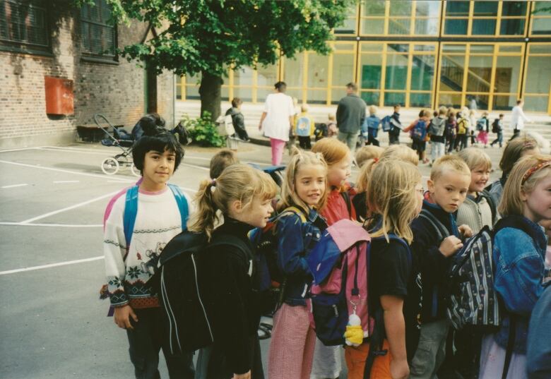 A young girl with a high pony tail behind a group of other kids in a school yard.