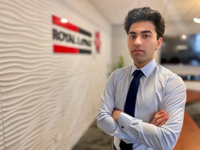 A man with a light blue shirt and tie standing in a real estate office.