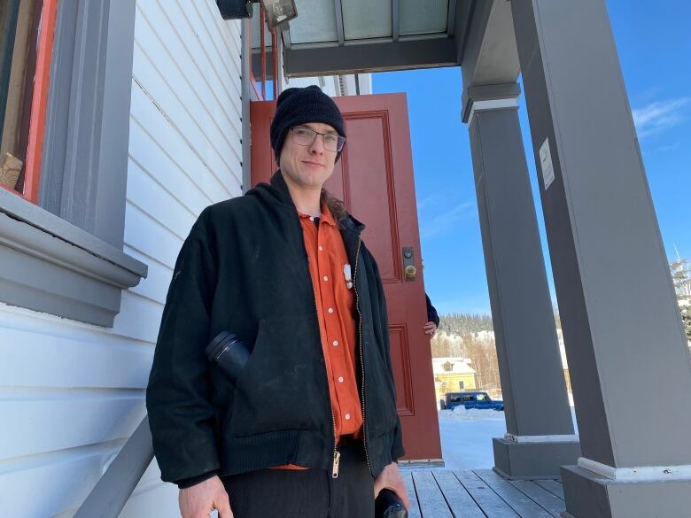 A man in a toque stands on some steps near the front entrance to a building.