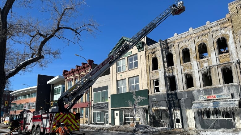 A ladder truck sits in front of a burnt-out brick building covered in ice in the daytime.