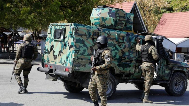 Men wearing military gear stand beside a vehicle.