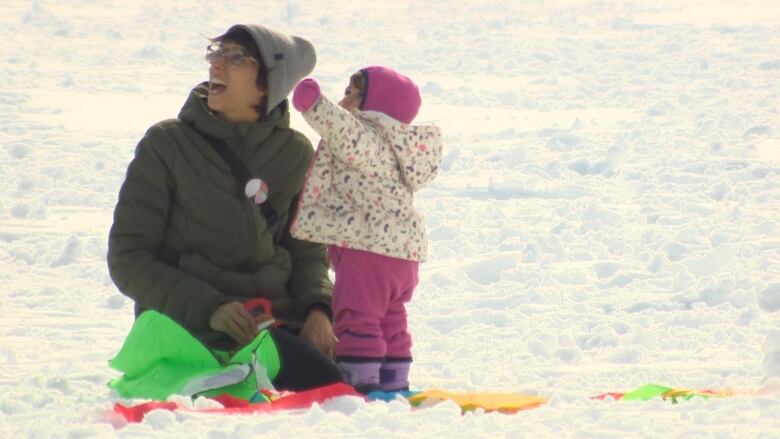 A picture of an adult on her knees looking up, next to a young kid pointing at the sky.