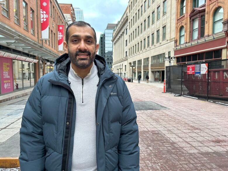 A man in a blue coat stands on a street.