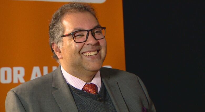 A man wearing a suit smiles in front of a backdrop.