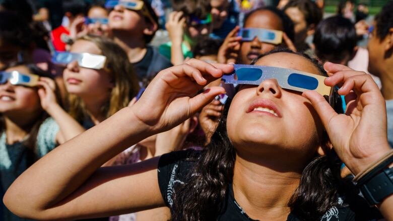 A girl holds paper eye glasses to her eyes.