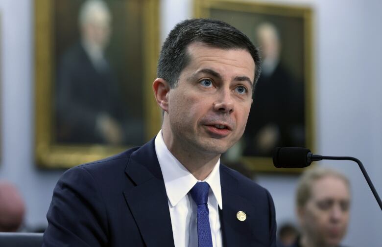 A man in a suit sits at a microphone.