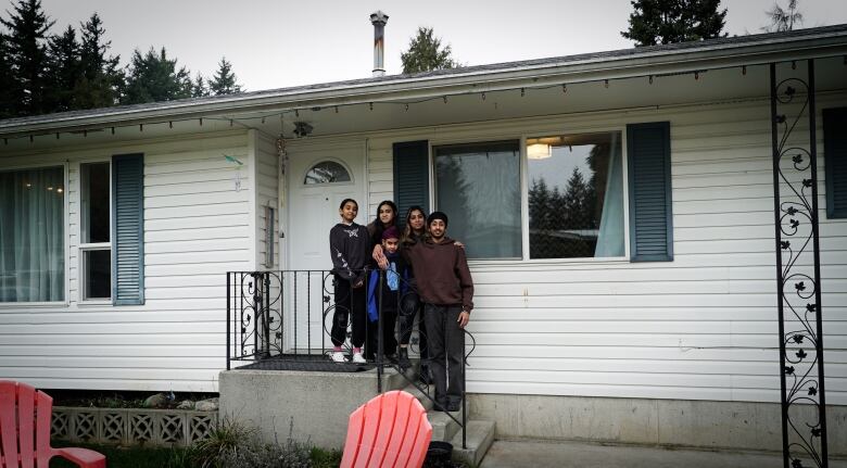 Five kids stand infront of their white home with blue shutters. 