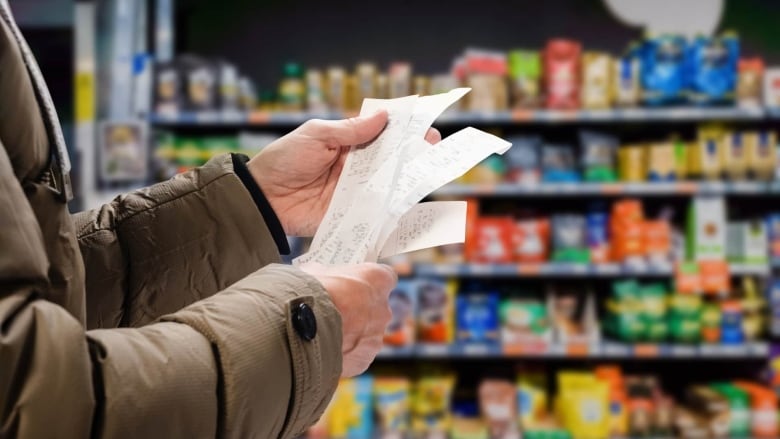 A closeup of hands holding receipts. A grocery aisle is seen in the background.