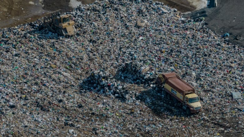 An aerial view of piles of colourful garbage, with a brown truck tipping out a fresh load