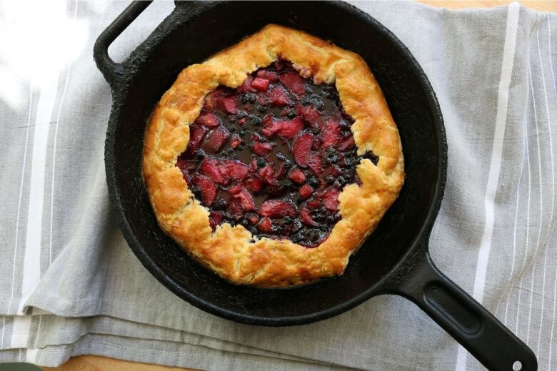 a berry and rhubarb pie is pictured in a black cast iron skillet.