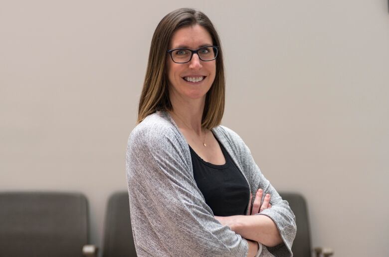 A woman with brown hair and glasses, wearing a black shirt and grey cardigan.