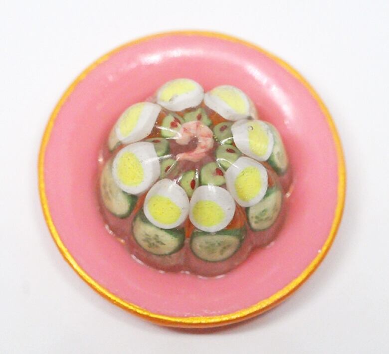 Little jelly salad with egg and cucumber on a pink plate with a gold rim.