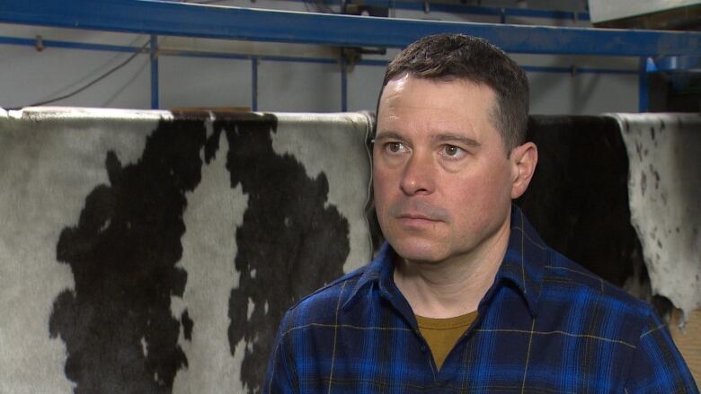 A man wearing blue plaid sits in front of drying seal pelts. 