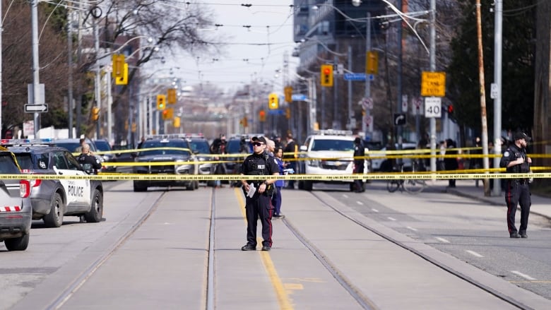 Police officers behind yellow caution tape on a busy street.