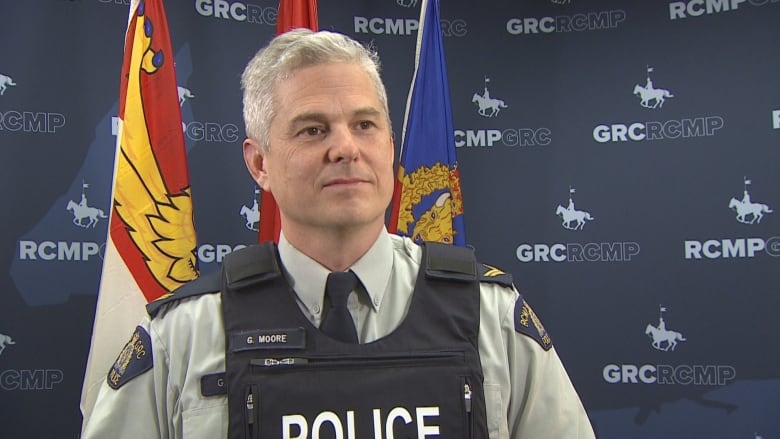 A police officer wearing a vest stands in front of flags.