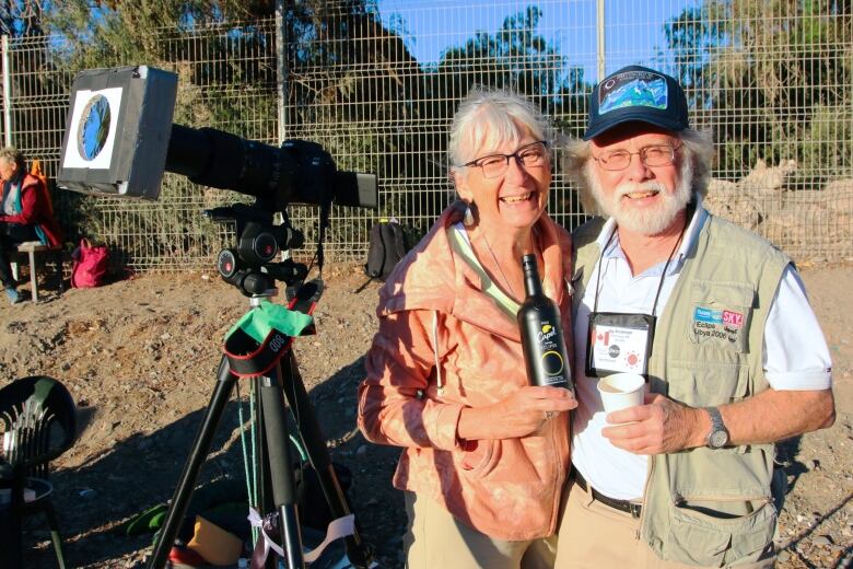 A man and a woman pose next to a camera equipped with a solar filter.