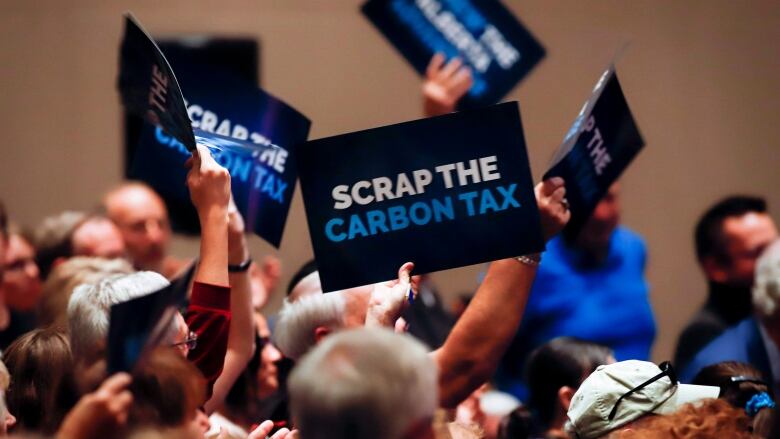 People wave signs during an anti-carbon tax rally in Calgary on Friday, Oct. 5, 2018.