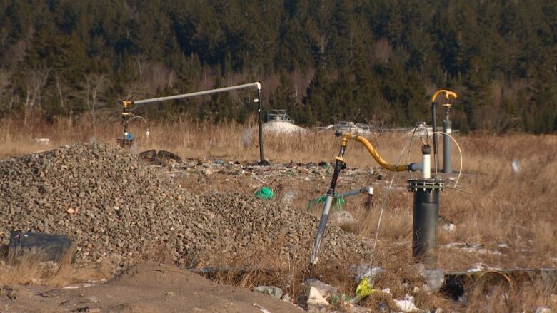 Pipes and hoses poking out of the ground. Beside and around the pipes are piles of gravel and some loose garbage. 