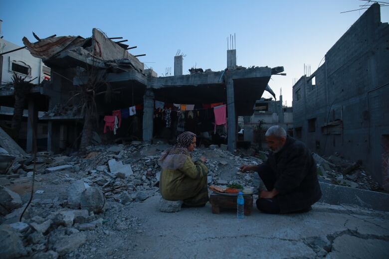 A man and a woman eat on a table on rubble in Gaza 