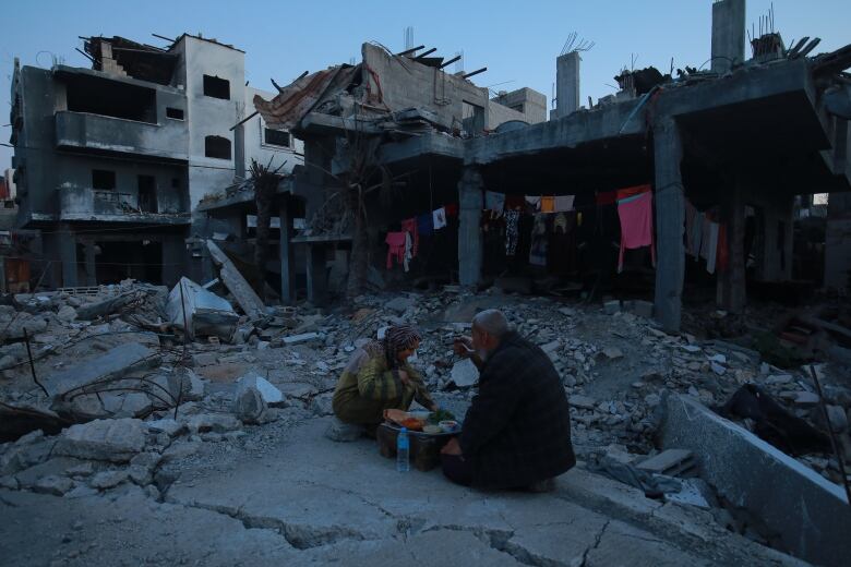 A man and a woman eat at a table on top of rubble.