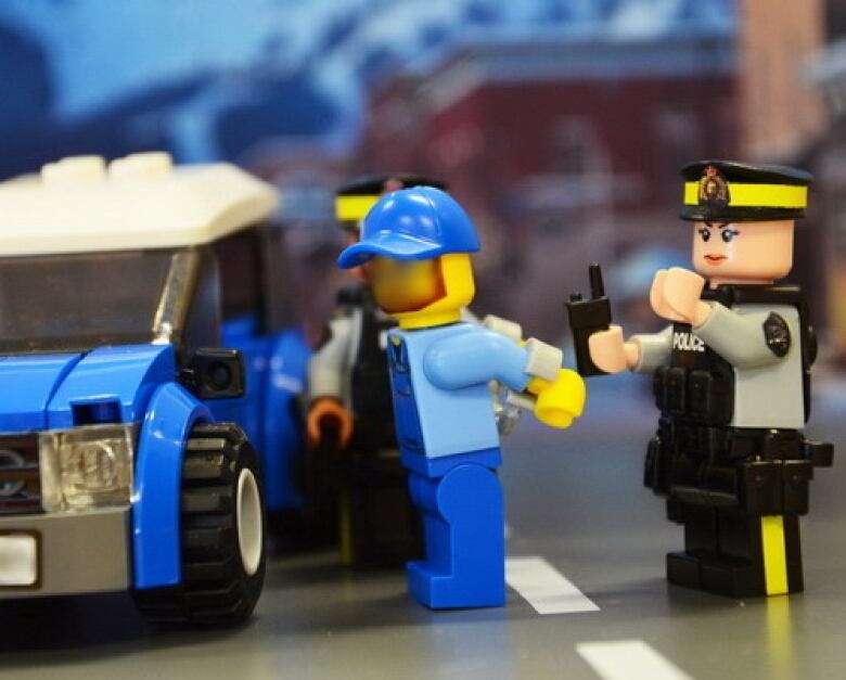 A toy lego police officer arrests a lego man. 