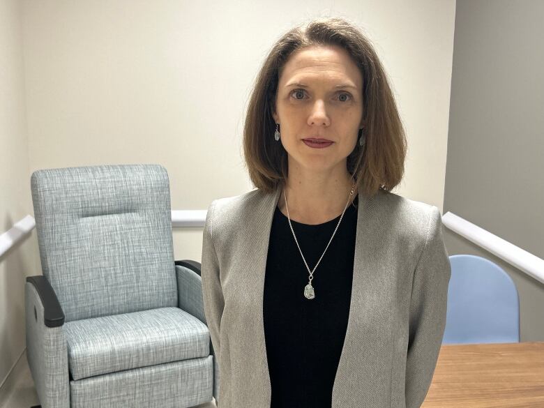 A woman stands in an office with a table and armchair behind her. 