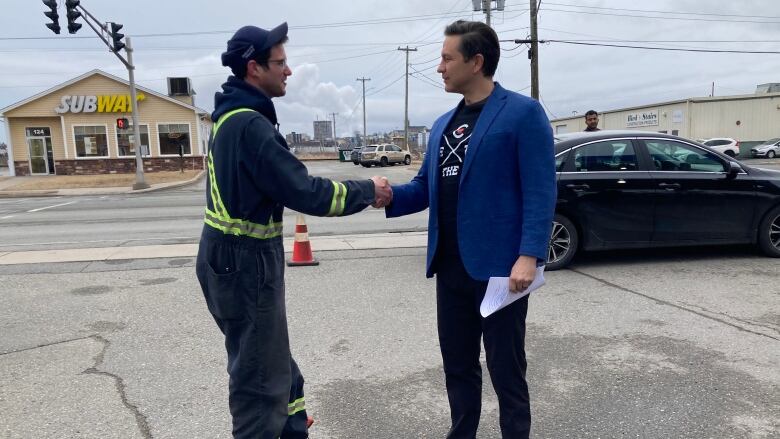 Pierre Polievre shakes hands with a man in workers coveralls 