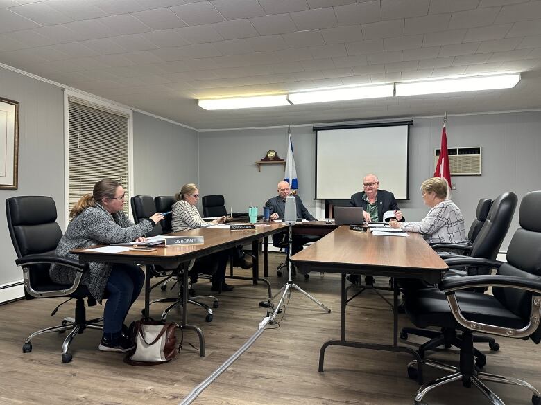 A group of people sit around a council chamber table. 