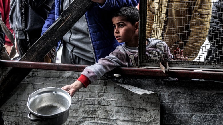 A young child holds out an empty pot at a barricade.