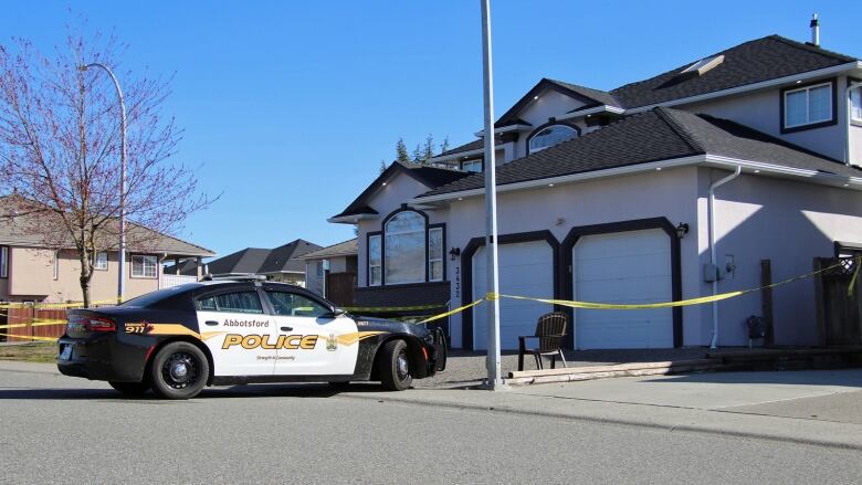 A police car standing in front of a house, access blocked with yellow tape. 