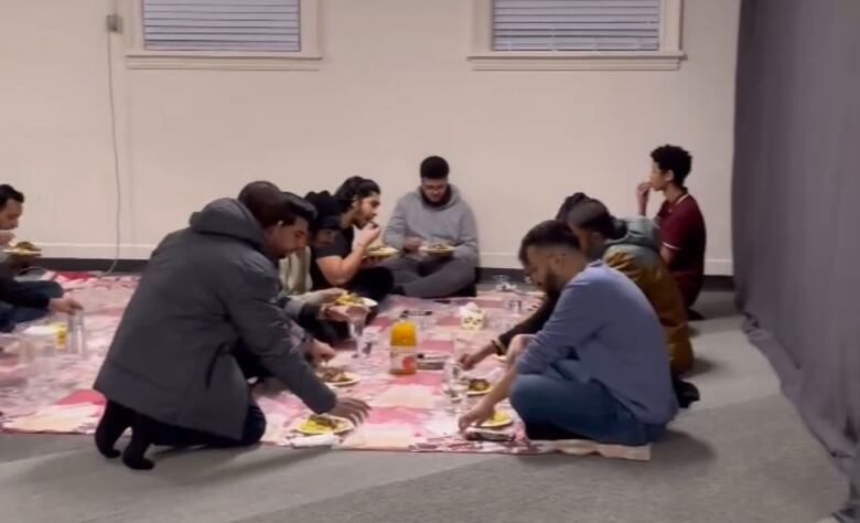 People sitting on a blanket, eating.