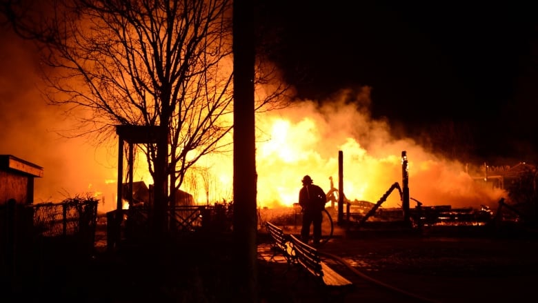 A fire eats away at a building. A firefighter is seen holding a hose.