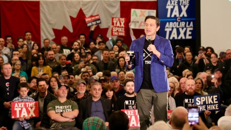 a politician stands on a stage with a crowd around him. He holds a beer. Supporters hold signs that say 'axe the tax' and spike the hike' 