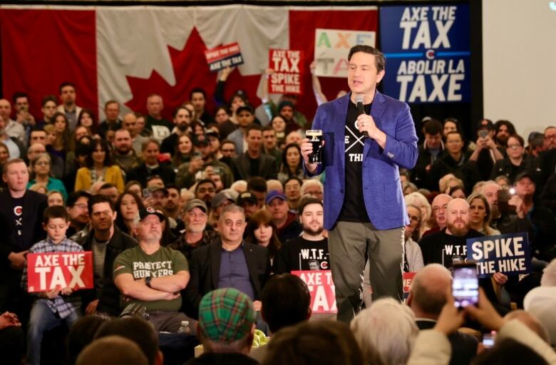 a politician stands on a stage with a crowd around him. He holds a beer. Supporters hold signs that say 'axe the tax' and spike the hike' 