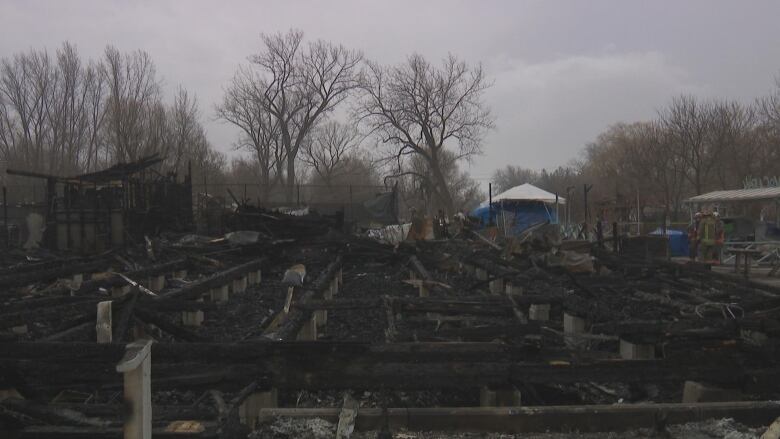 What's left of a building after a devastating fire. Firefighters are seen grouped up in the background. 