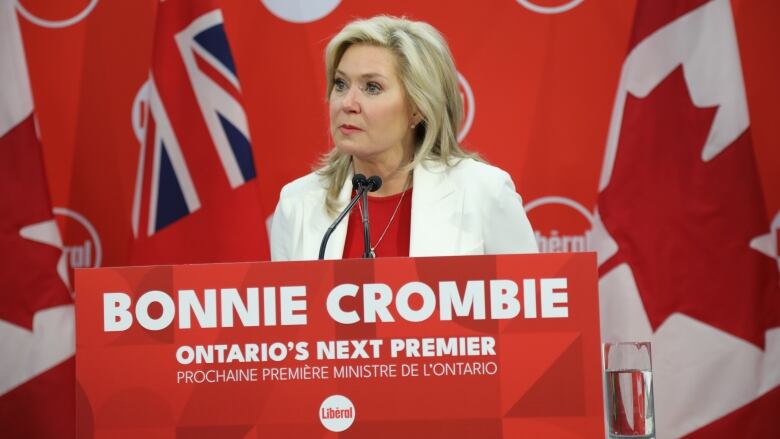 A woman stands at a podium. A sign underneath her reads 