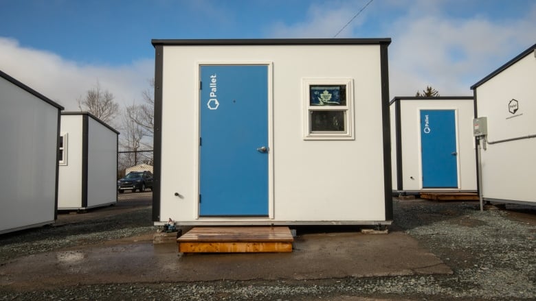 A closeup of the front of a small hut-like structure with white walls, a blue roof and a single window next to a blue front door.