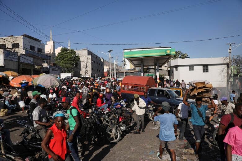 A large crowd of pedestrians and people on scooters gather around a gas station.